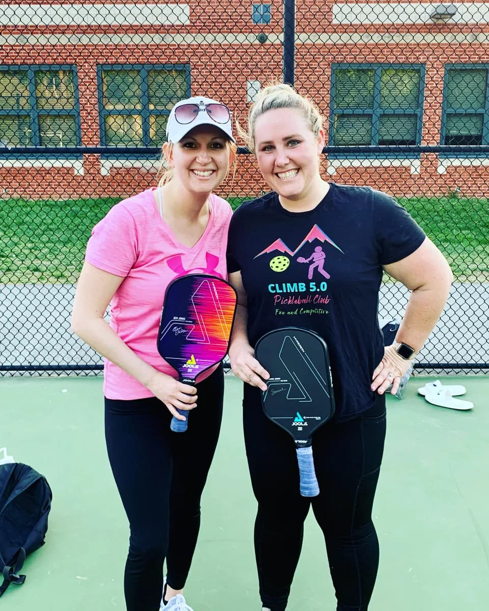 Two pickleball players smiling with their paddles beside an outdoor court