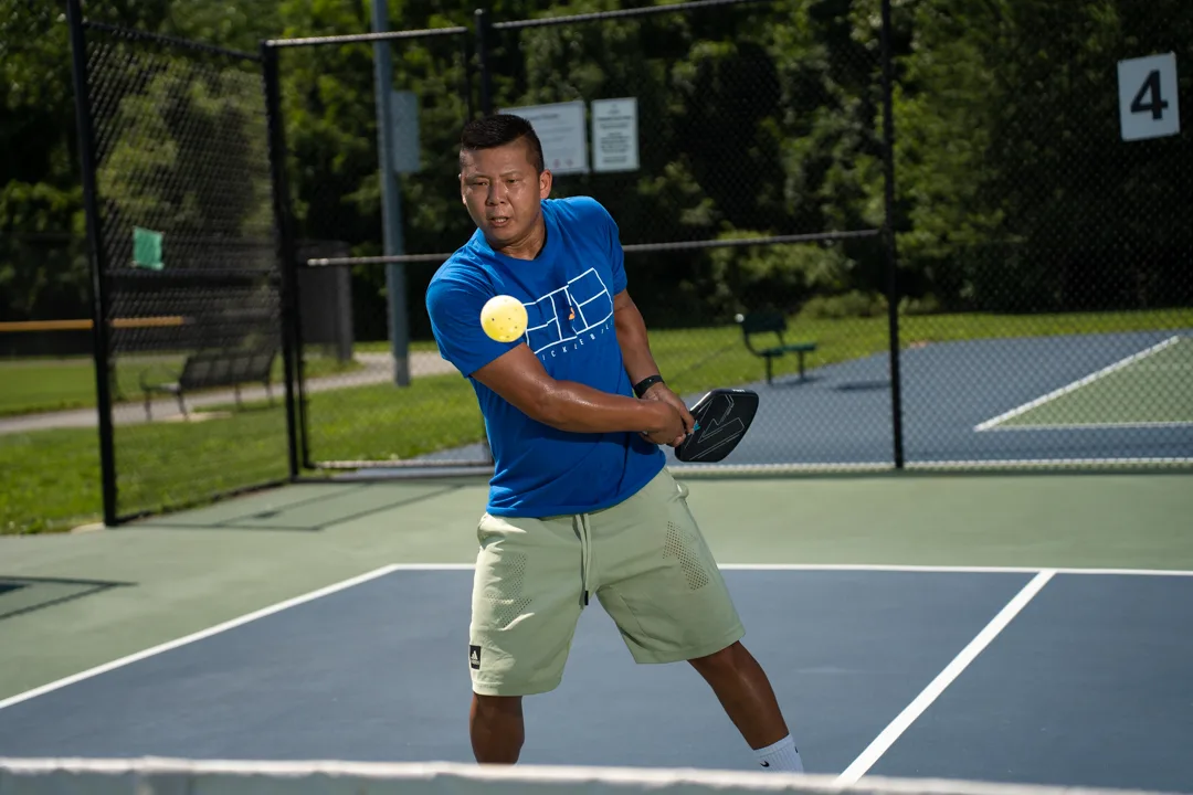 Sam Morris holding his paddle near a yellow pickleball on an outdoor court