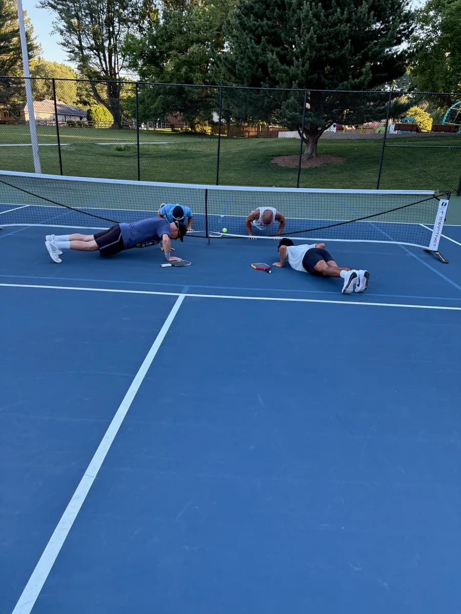 Four adult pickleball players doing pushups beside an outdoor net