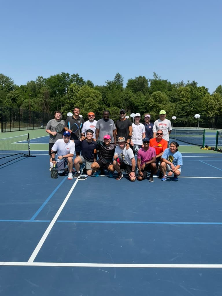 A smiling group of pickleball players with paddles on an outdoor court