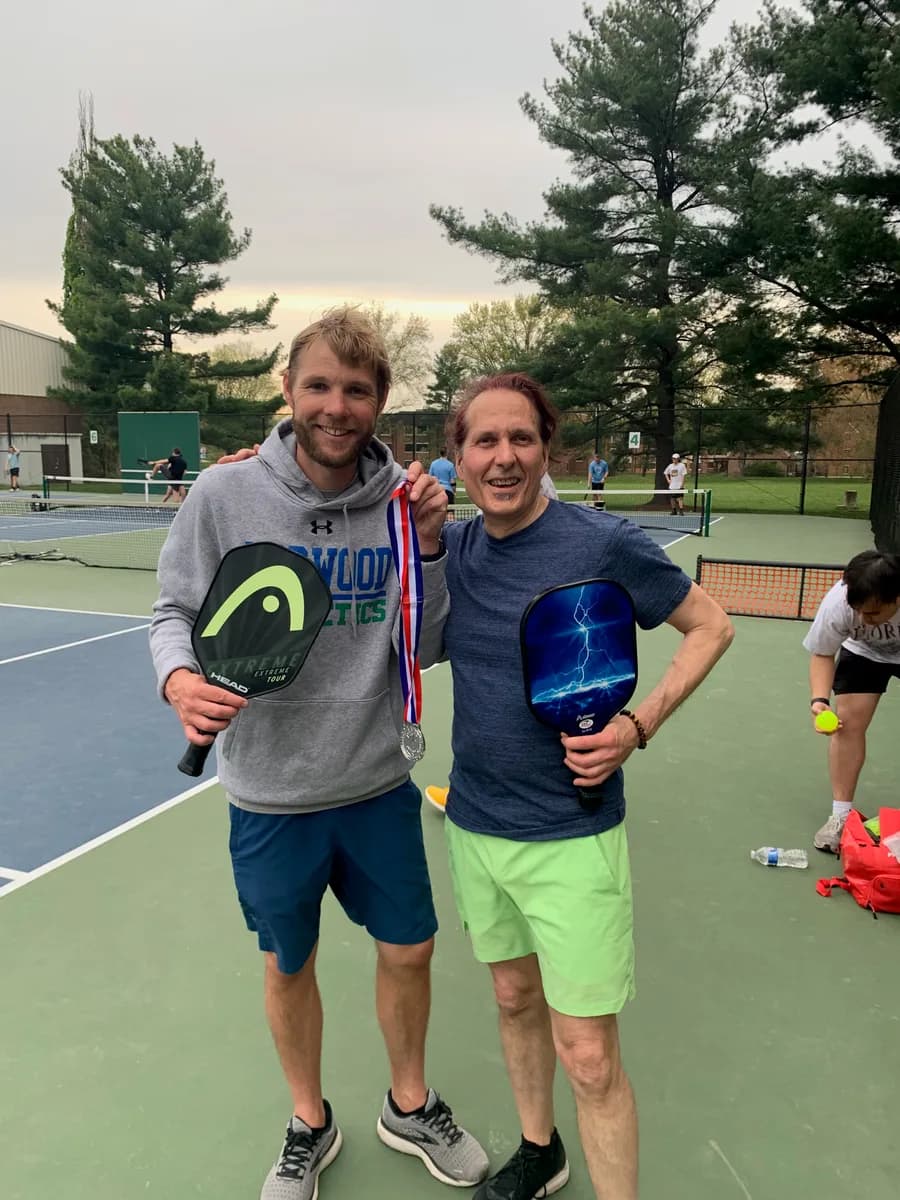 Pickleball players smiling and holding their paddles beside the court