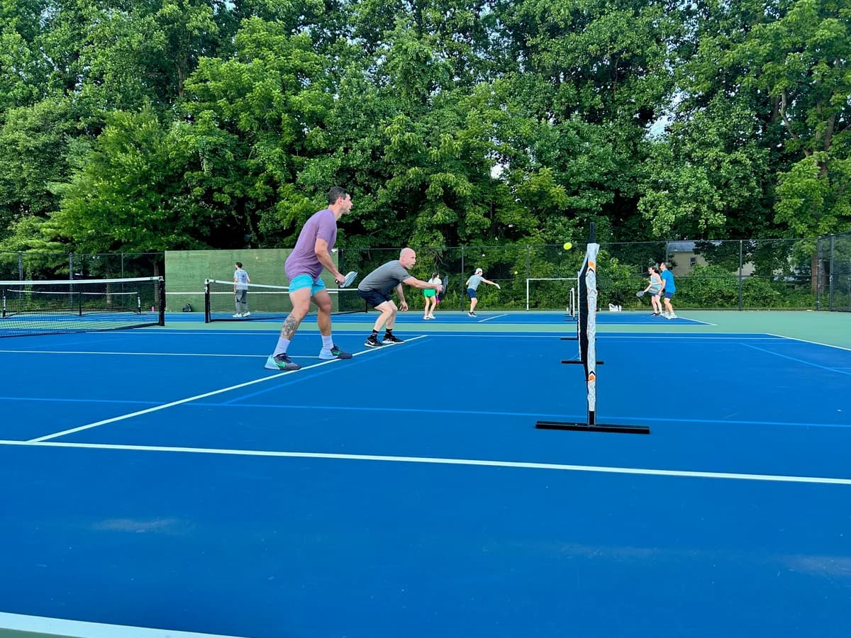 Pickleball players preparing for or playing a doubles rally on outdoor courts