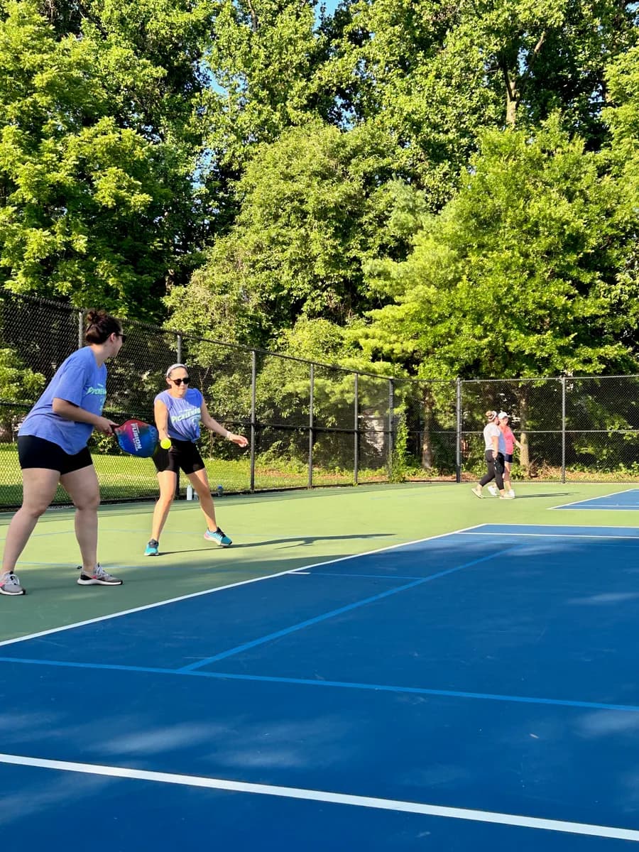 Pickleball players preparing for or playing a doubles rally on outdoor courts