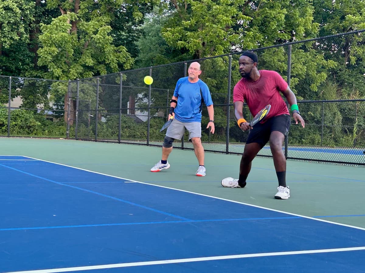 Pickleball players preparing for or playing a doubles rally on outdoor courts