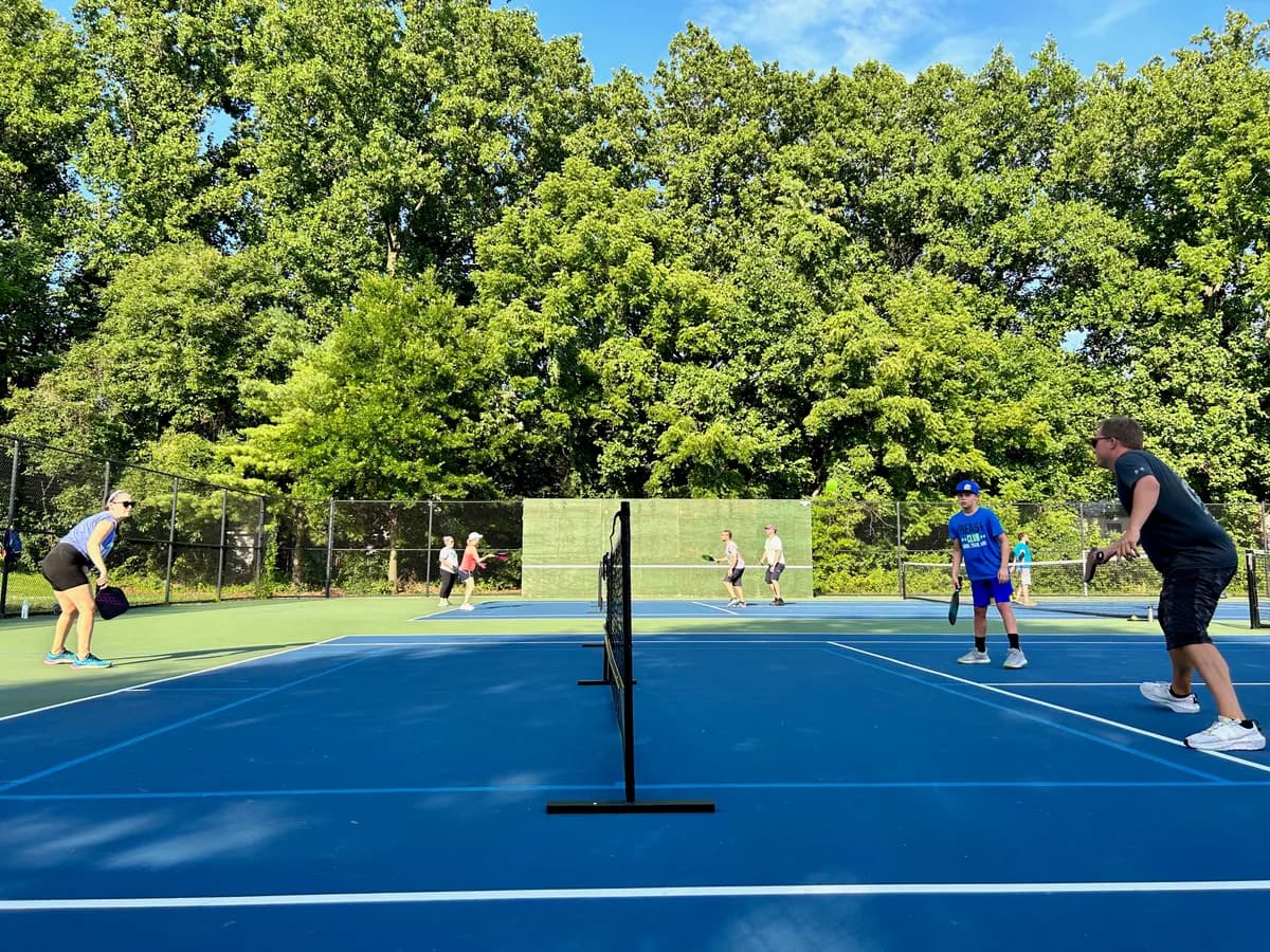 Pickleball players preparing for or playing a doubles rally on outdoor courts