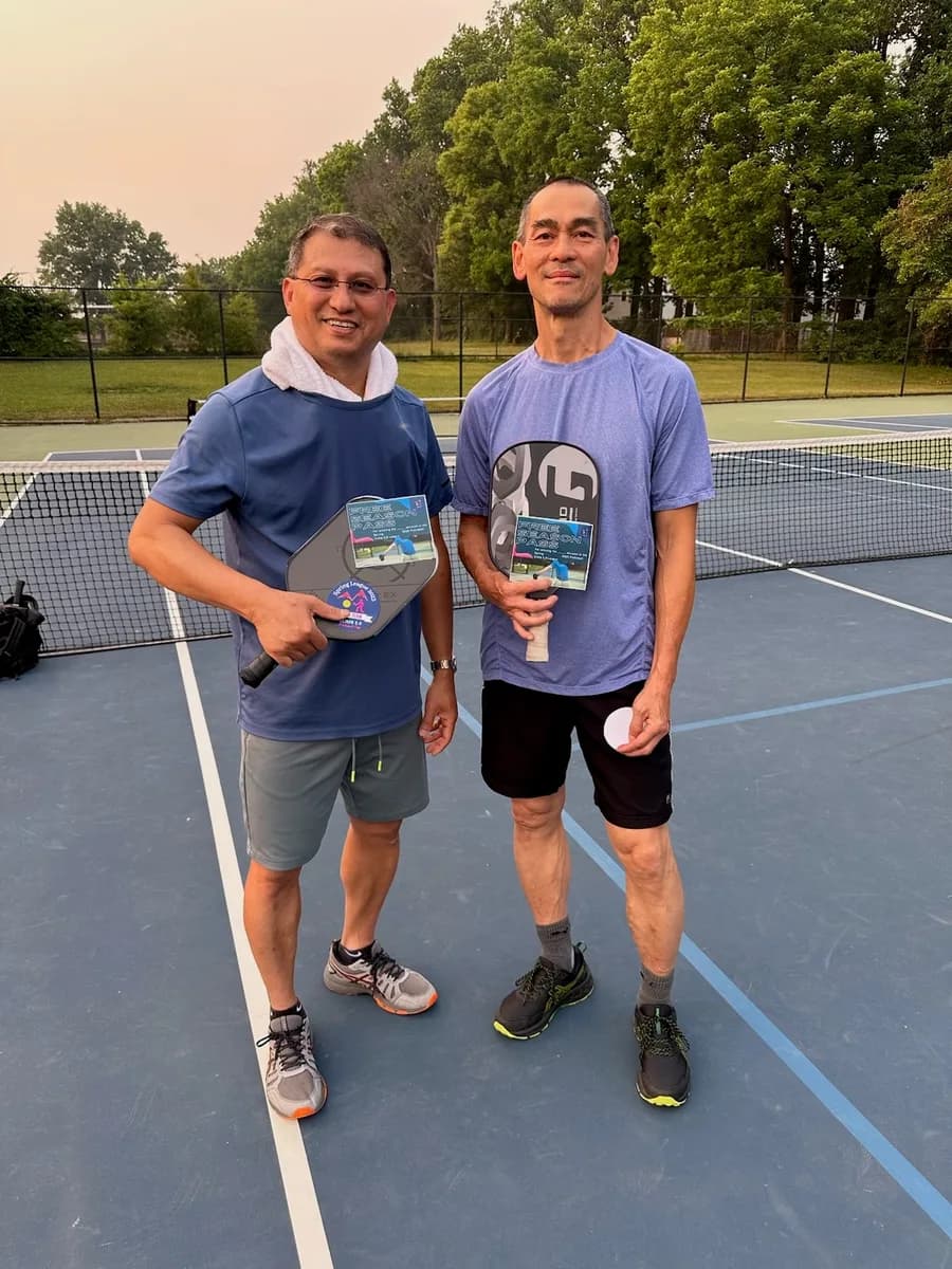 Pickleball players smiling and holding their paddles beside the court