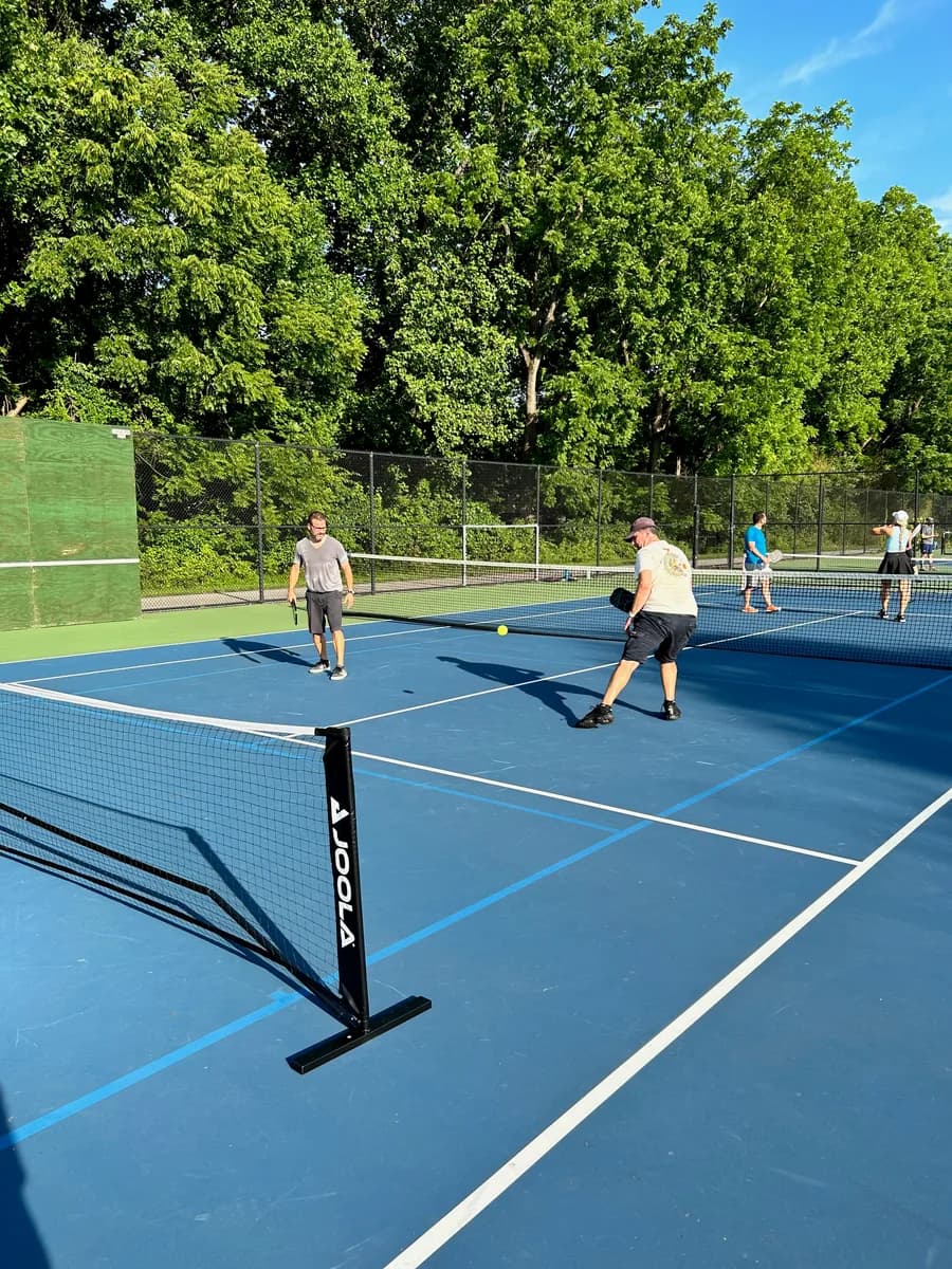 Pickleball players preparing for or playing a doubles rally on outdoor courts