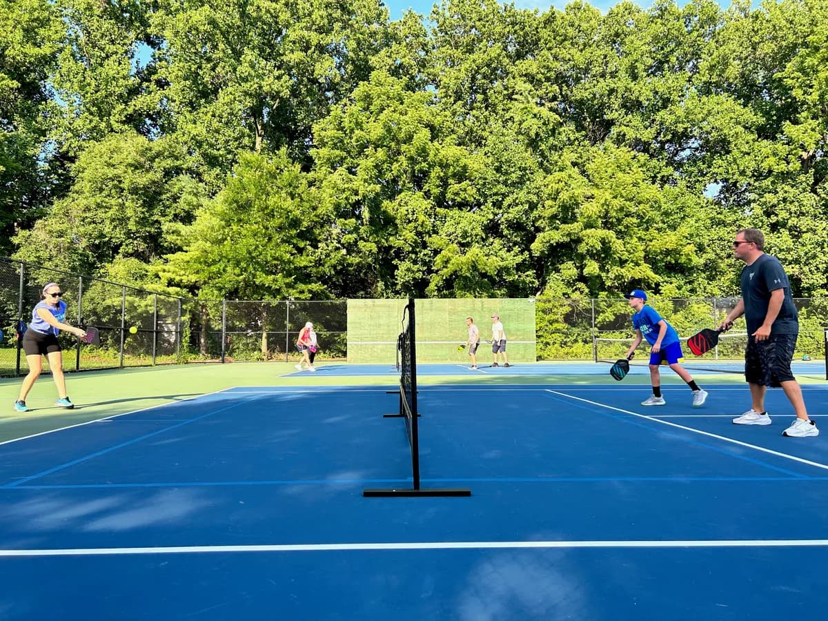 Pickleball players preparing for or playing a doubles rally on outdoor courts