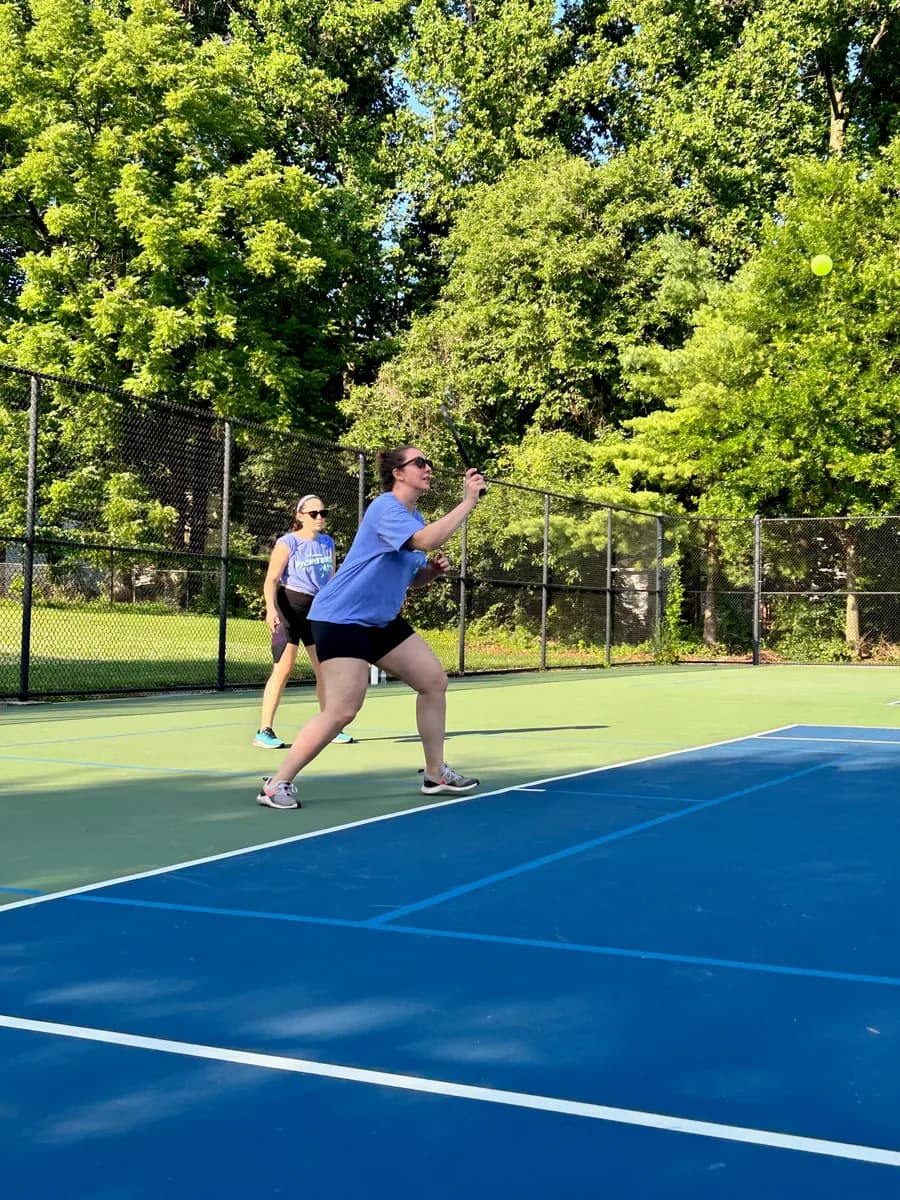 Pickleball players preparing for or playing a doubles rally on outdoor courts