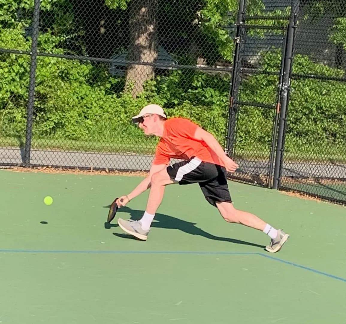 A pickleball player reaching toward a yellow ball on an outdoor court