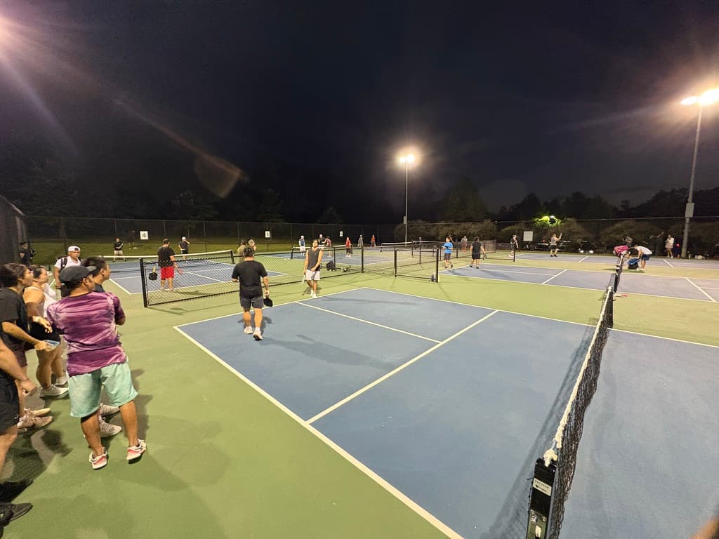 Players sharing outdoor pickleball courts under evening lights