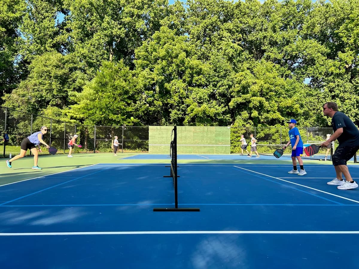 Pickleball players preparing for or playing a doubles rally on outdoor courts