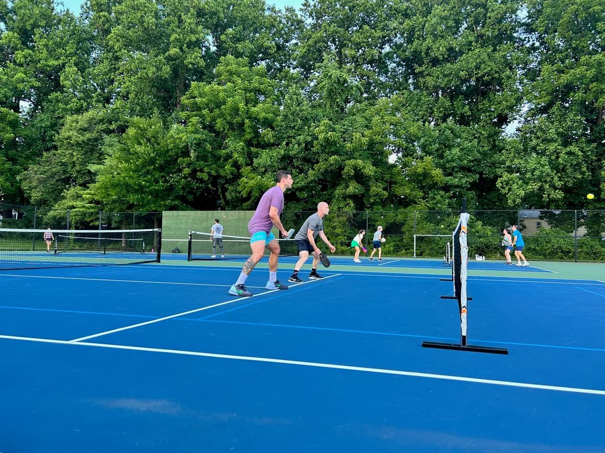 Pickleball players preparing for or playing a doubles rally on outdoor courts