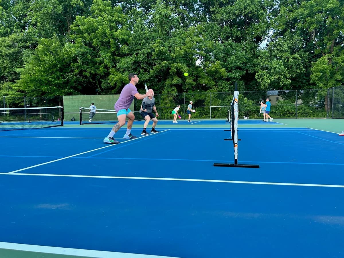 Pickleball players preparing for or playing a doubles rally on outdoor courts