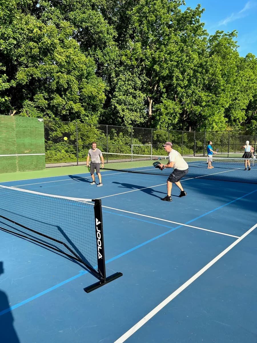 Pickleball players preparing for or playing a doubles rally on outdoor courts