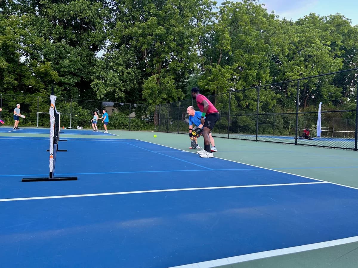 Pickleball players preparing for or playing a doubles rally on outdoor courts