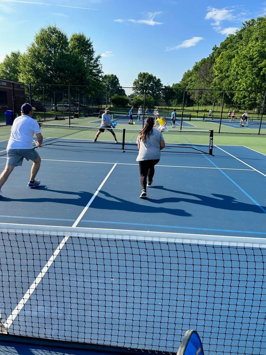 Pickleball players preparing for or playing a doubles rally on outdoor courts
