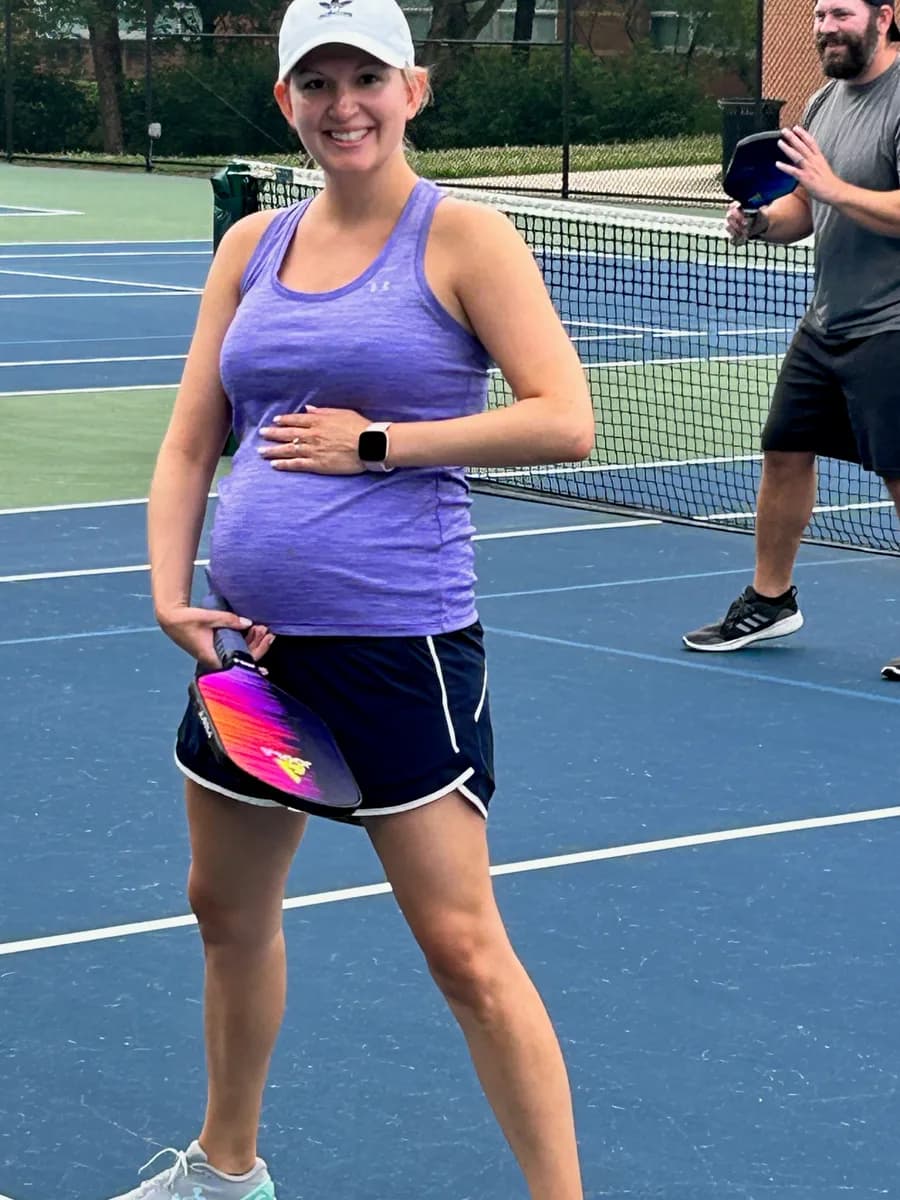 A pickleball player smiling with a paddle beside an outdoor net